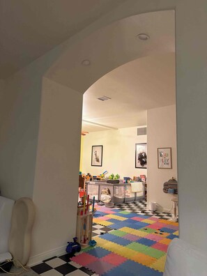 Un couloir mène à une salle de jeux où l’on trouve des tapis en mousse colorés et des jouets.