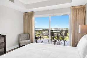 Ein Hotelzimmer mit einem großen Bett, einem Sessel, einem Tisch mit Stühlen und Blick auf das Meer und die Gebäude.