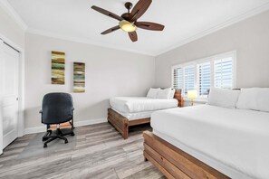 Ein Schlafzimmer mit Deckenventilator, zwei Betten, einem Schreibtisch und einem Fenster mit Jalousien.