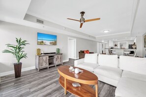 A modern living room with a white sofa, a wooden coffee table, and a ceiling fan. - Habor Landing 402B harbor views nearby beach access (Destin)