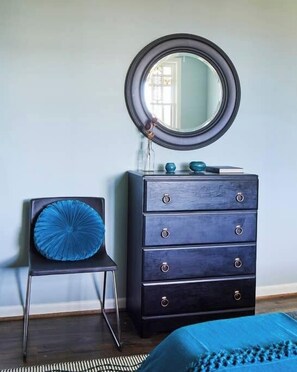 Ein Zimmer mit einem dunkelblauen Kommode, einem runden Spiegel und einem blauen Sessel mit passender Sitzkissen.