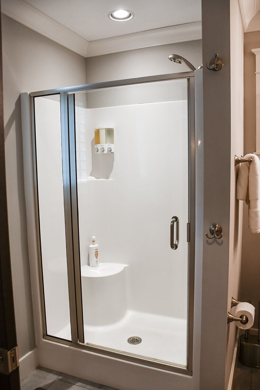Une douche à l’italienne avec une porte en verre, un porte-serviettes et un support à rouleau de papier toilette.