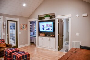 A room with a television mounted on a wall, a wooden table, and a bench with plaid cushions.