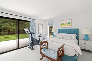 Un dormitorio con cama, una silla, una mesita de noche, una lámpara, una ventana y una bicicleta estática.