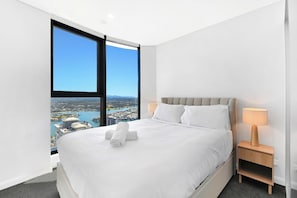 Een moderne hotelkamer met een groot bed, een nachtkastje met een lamp en een stadsgezicht door een groot raam.
