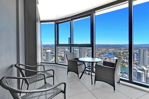 Een balkon met uitzicht op een stadsgezicht, gemeubileerd met rieten stoelen en een tafel.