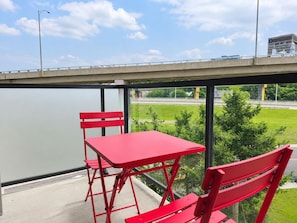 Ein rotes Tisch- und Stuhlgarnitur auf einem Balkon mit Blick auf eine Brücke und Grünflächen.