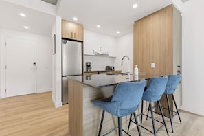 A modern kitchen with a central island, bar stools, and a stainless steel refrigerator. - Flight 23 – Urban Stay | Rooftop Pool | Sleeps 8 (Québec)