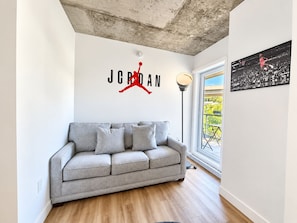 Ein Wohnzimmer mit grauem Sofa, Jordan-Logo an der Wand, einer Stehlampe und einem großen Fenster.