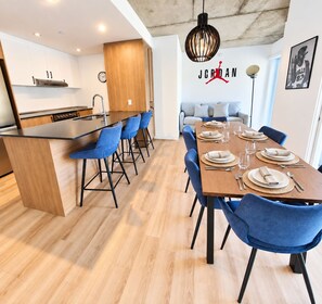 Eine moderne Küche mit einer Holztheke, blauen Barhocker und einem Essbereich mit einem langen Tisch, gedeckt für sechs Personen.