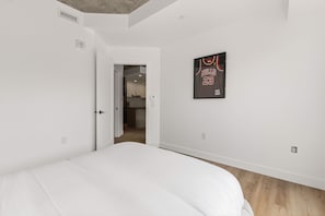 A bedroom with a bed, a door leading to a kitchen, and a framed Bulls jersey on the wall. - Flight 23 – Urban Stay | Rooftop Pool | Sleeps 8 (Québec)