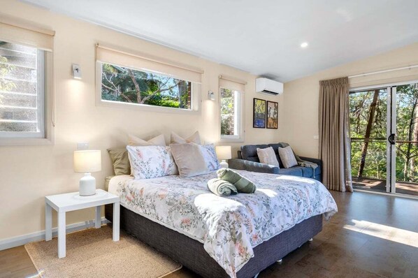 A bedroom with a large bed, a nightstand, a sofa, and a view of the outdoors.