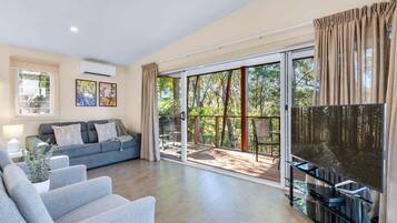 A living room with a sofa, a flat-screen TV, and a sliding glass door leading to an outdoor area.