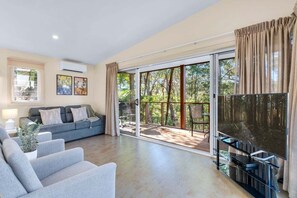 A living room with a sofa, a flat-screen TV, and a sliding glass door leading to an outdoor area.