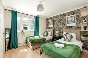 A bedroom with two beds, green bedding, a window with curtains, a radiator, and wall art. - 2-Bed Kennington House with Parking and Garden (Greater London)