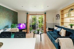 A living room with a TV, sofa, coffee table, and a view through a glass door to the outdoors. - 2-Bed Kennington House with Parking and Garden (Greater London)