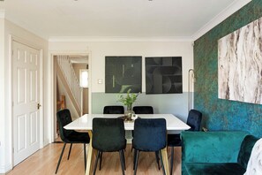 A dining area with a white table, black chairs, and a green sofa. There are abstract wall art pieces above the table. - 2-Bed Kennington House with Parking and Garden (Greater London)