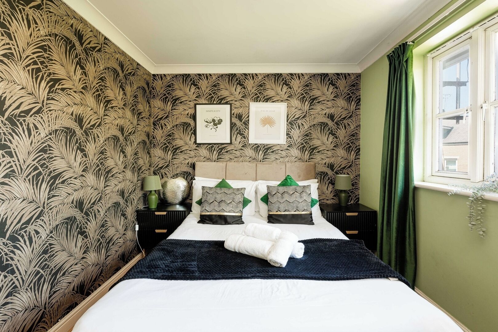 A bedroom with a bed, two nightstands, a window with curtains, and a wall with a leaf pattern.