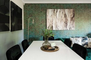 A dining area with a white table, black chairs, a vase with a plant, and a remote control on a tray. - 2-Bed Kennington House with Parking and Garden (Greater London)