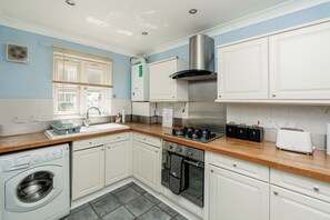 A compact kitchen with a built-in washing machine, a stove, and a sink. - 2-Bed Kennington House with Parking and Garden (Greater London)