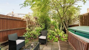 Eine Terrasse mit Korbmöbeln, einem Grill und verschiedenen Pflanzen.