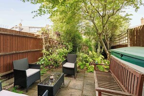 A patio area with wicker furniture, a barbecue grill, and a variety of plants. - 2-Bed Kennington House with Parking and Garden (Greater London)