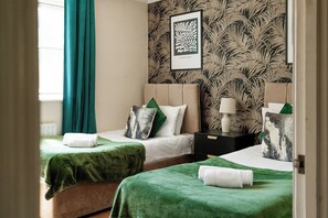 A hotel room with two beds, green bedspreads, a framed artwork on the wall, and a window with curtains. - 2-Bed Kennington House with Parking and Garden (Greater London)