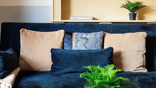 Ein Wohnzimmer mit einem dunkelblauen Sofa, einem Glastisch und einem Bücherregal mit Dekoration.