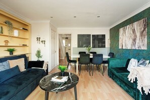 Ett modernt vardagsrum med en svart soffa, ett soffbord i glas och en soffa i turkos. Här finns också en matplats med ett vitt bord och svarta stolar.