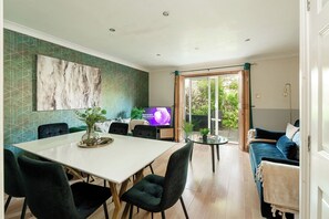 A modern living room with a dining area, a television, and a view of the outdoors. - 2-Bed Kennington House with Parking and Garden (Greater London)