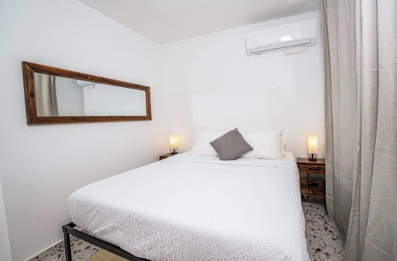 Une chambre à coucher comprenant un lit, une table de chevet avec une lampe, un miroir fixé au mur et un appareil de climatisation.