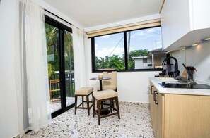 A compact kitchen with a dining area, a large window, and a view of greenery outside. - Seaside Sanctuary: Bright & Airy 2BR by the Beach (Vega Alta)