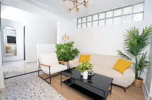 Een moderne woonkamer met een bank, fauteuil, salontafel en potplanten.