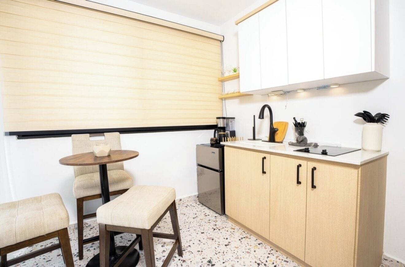 A compact kitchen with a round table, two chairs, a countertop with a sink, and a stove.