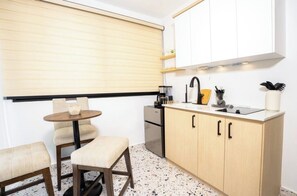 Een kleine keuken met een ronde tafel, twee stoelen, een aanrecht met een spoelbak en een fornuis.