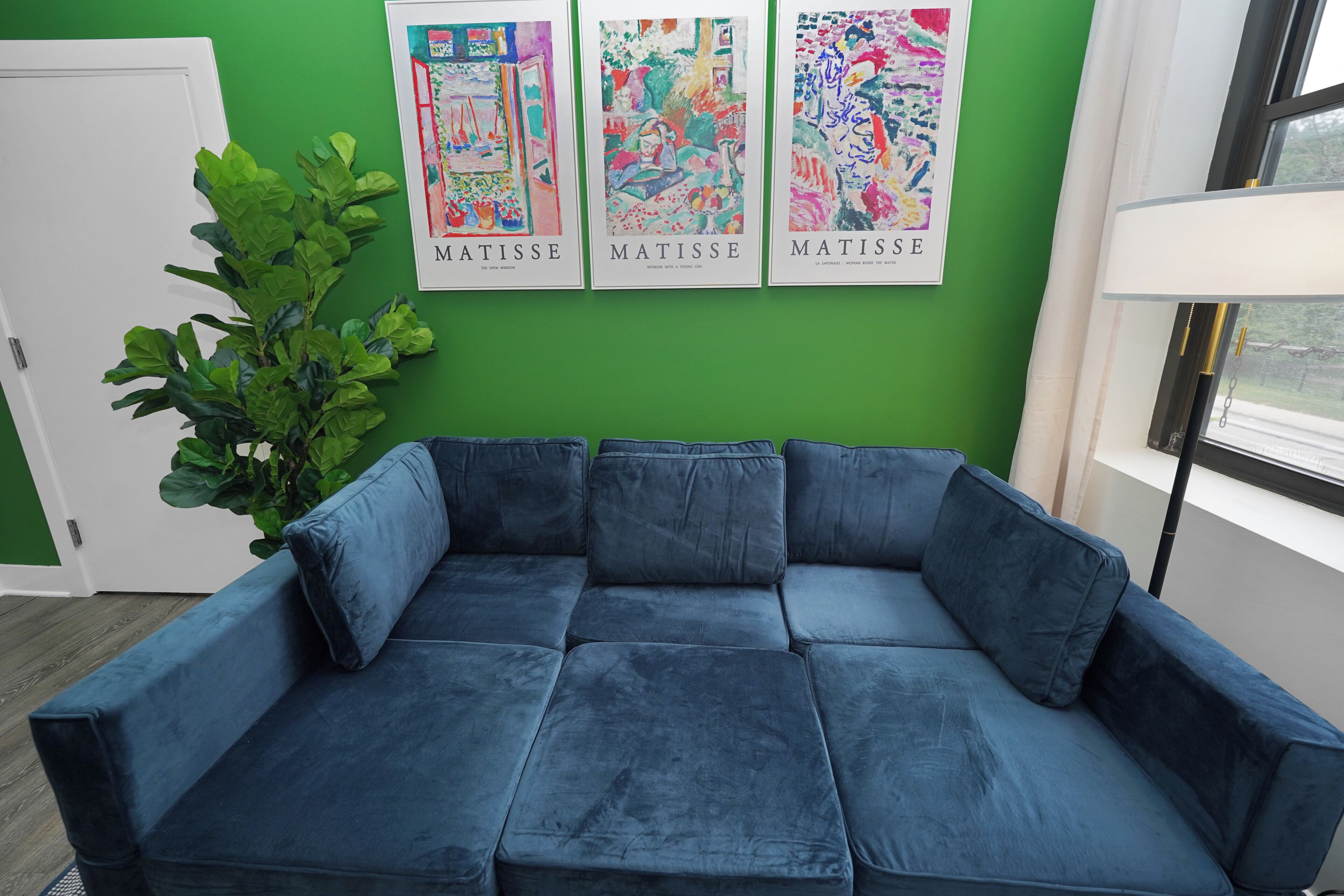 Une pièce avec un canapé d’angle bleu, une grande plante verte et trois œuvres d’art encadrées accrochées au mur.