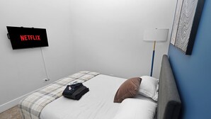 A hotel room with a bed, a TV mounted on the wall, a lamp, and a folded jacket on the bed. - Cozy 2BR Near McCormick & Wintrust with Optional Parking (Chicago)