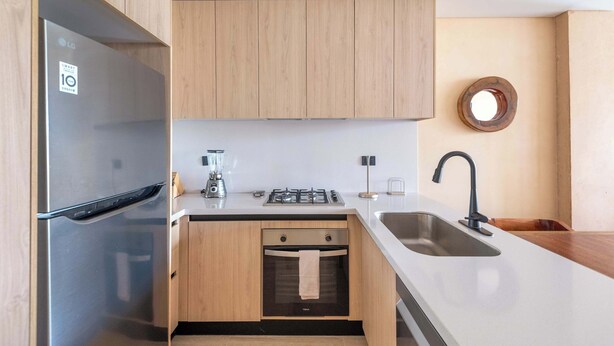 A modern kitchen with a stainless steel refrigerator, wooden cabinets, a gas stove, and a sink. - Elegant 2BR Condo at The Village Corasol (Playa del Carmen)