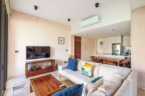 Ein modernes Wohnzimmer mit Flachbildfernseher, einer Couch, einem Couchtisch und einem Essbereich mit Holztisch und Stühlen.