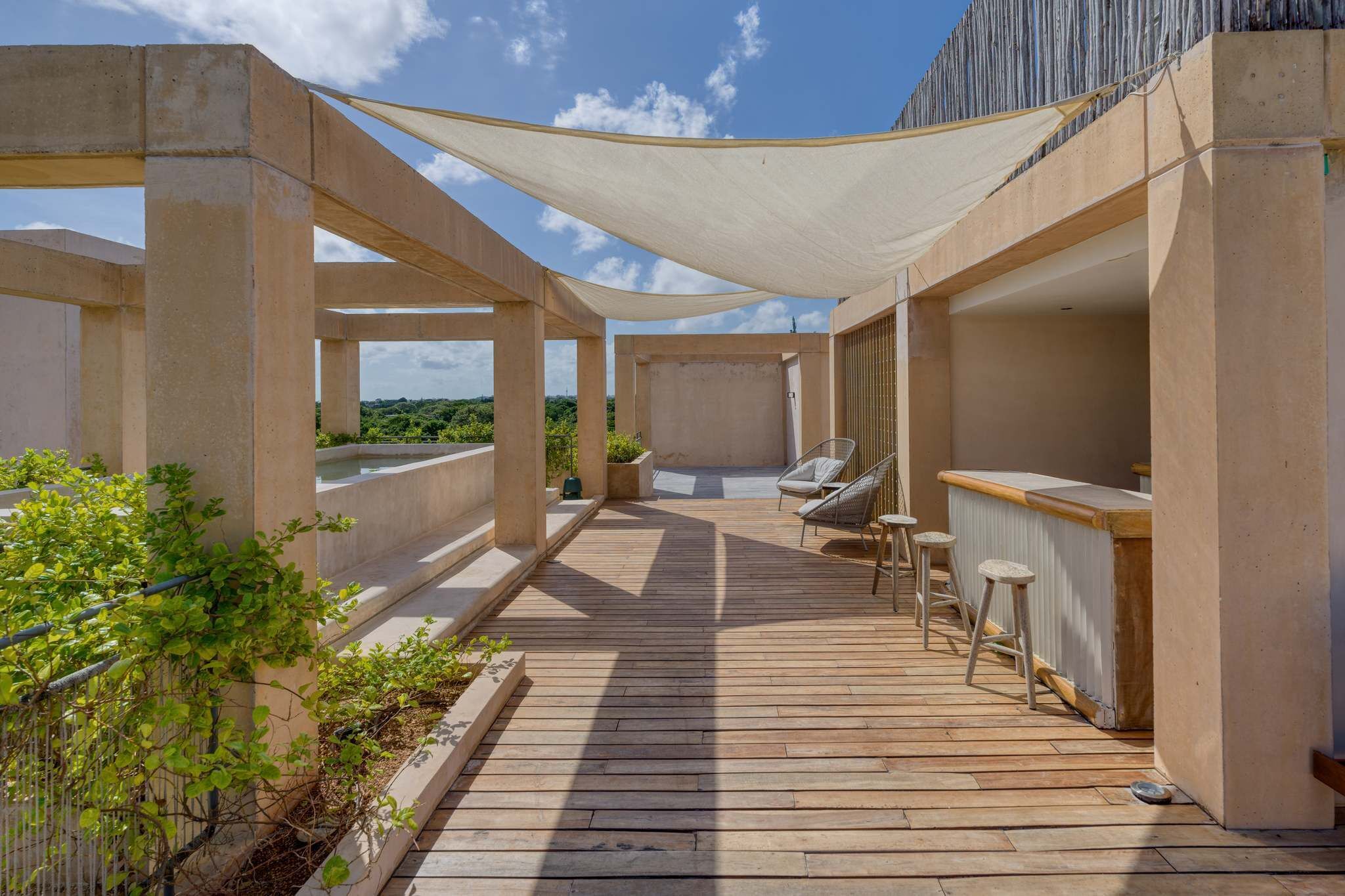 A wooden deck with a bar area, outdoor seating, and a view of greenery.