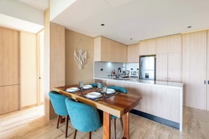 A modern kitchen with wooden cabinets, a central island, and a dining area with a wooden table and blue chairs. - Stylish 1BR Condo with Resort Amenities (Playa del Carmen)