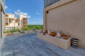 A rooftop terrace with a seating area, a row of vases, and a view of a building in the background. - Stylish 1BR Condo with Resort Amenities (Playa del Carmen)