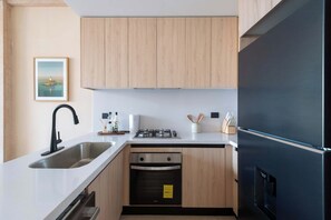 Eine moderne Küche mit Holzschränken, einer Edelstahl-Spüle, einem Gasherd und einem schwarzen Kühlschrank.