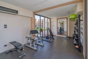 Ein Fitnessraum mit Trainingsgeräten, einer Bank und einer Spiegelwand.