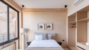 Een hotelkamer met een bed, nachtkastje, lamp, kledingkast en twee foto’s in lijsten aan de muur.