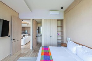 A modern hotel room with a bed, a TV, a kitchenette, and a bathroom. - Top-Floor 2BR PH at The Village Corasol (Playa del Carmen)