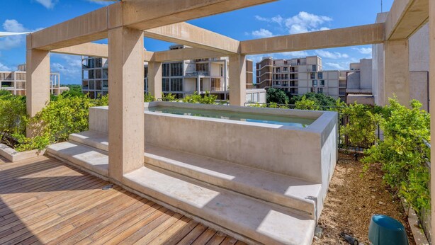 Eine Dachterrasse mit Pool, Betonbauten und umgebender Bepflanzung.