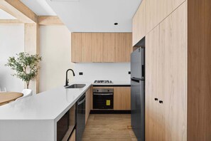 A modern kitchen with a white countertop, wooden cabinets, a stainless steel refrigerator, and a built-in oven. - 2BR Resort Condo near Beach & Golf (Playa del Carmen)