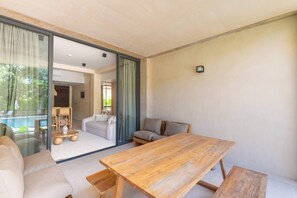 A modern interior with a wooden dining table, a sofa, and a view of a pool through a glass door. - 2BR Resort Condo near Beach & Golf (Playa del Carmen)