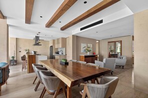 A spacious dining area with a long wooden table and upholstered chairs, a kitchen with modern appliances, and a living area with a sofa and a large mirror. - Bright 2BR Retreat near Golf & Beach (Playa del Carmen)